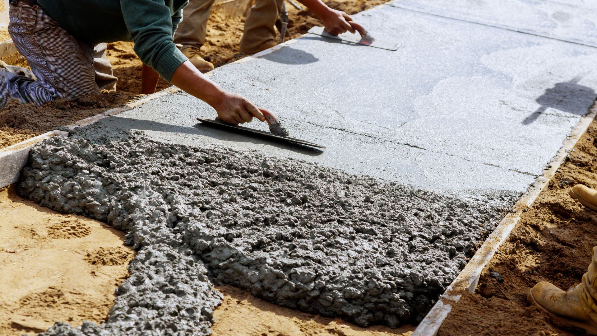 Worker smoothing wet concrete with trowel during sidewalk construction