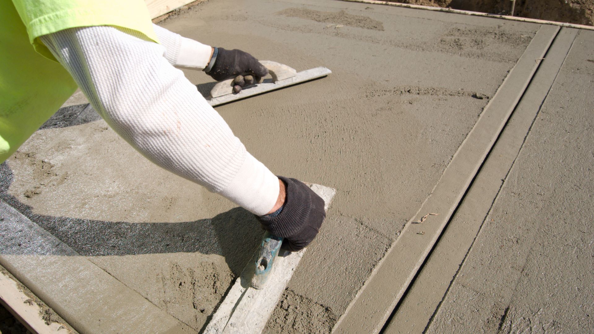 Construction worker smoothing wet concrete with trowel on job site