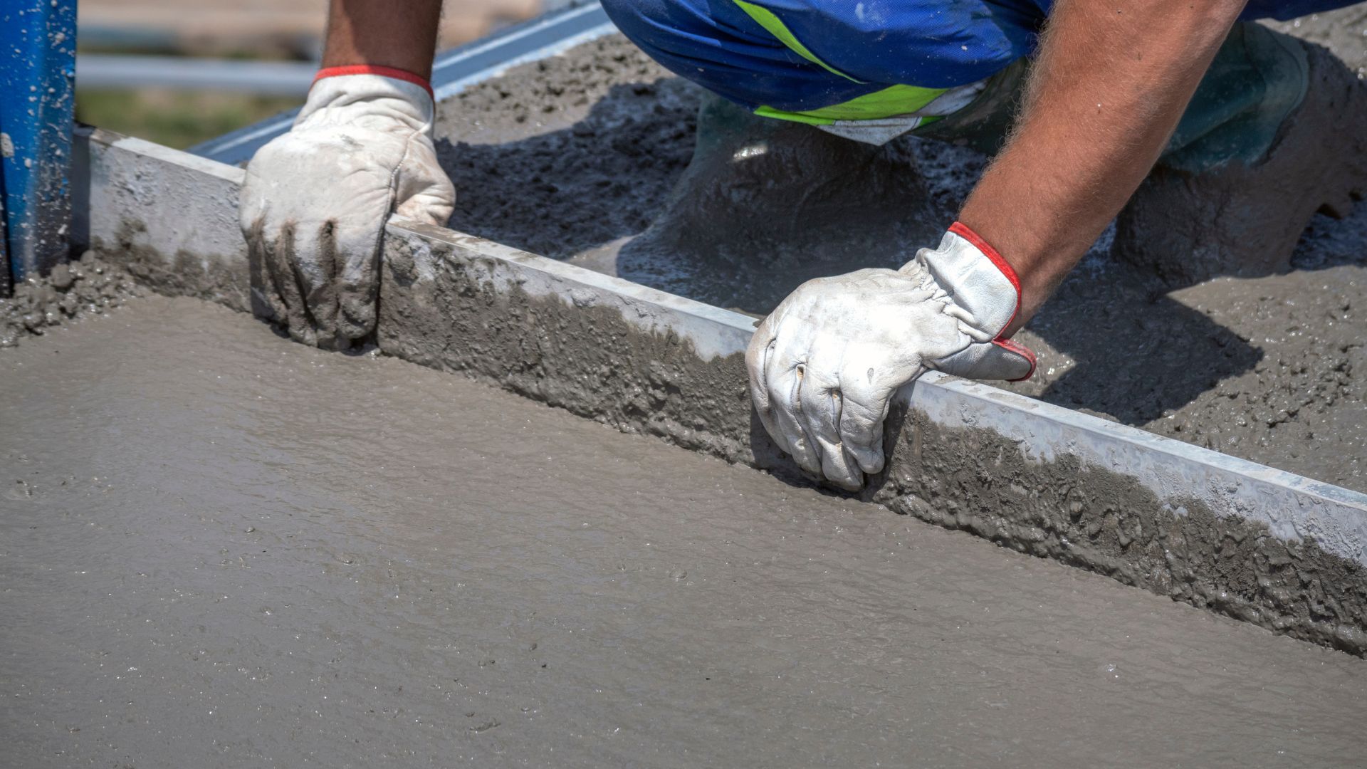 Worker smoothing wet concrete with leveling tool and protective gloves