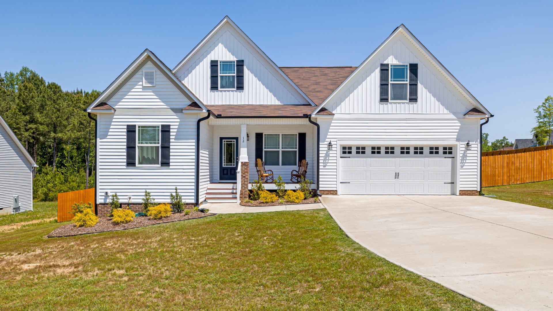 White two-story house with two-car garage, yellow flowers, and wooden fence