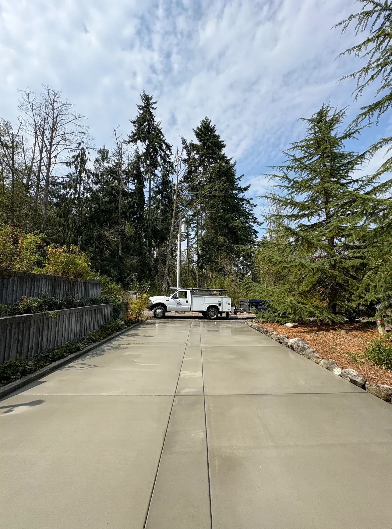 White service truck parked on concrete driveway surrounded by evergreen trees