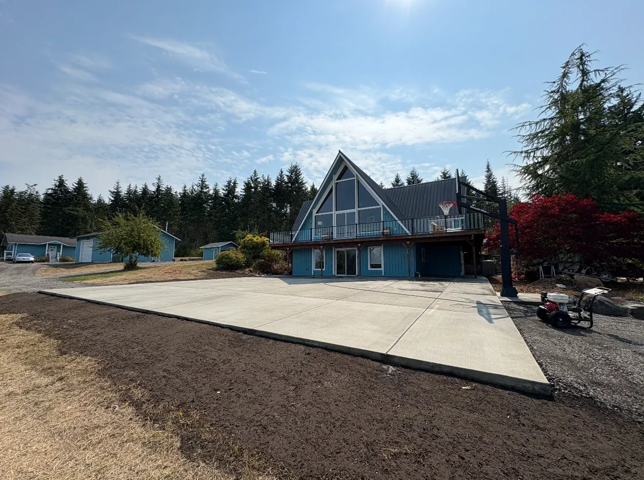 Blue A-frame house with large concrete driveway and pine forest background