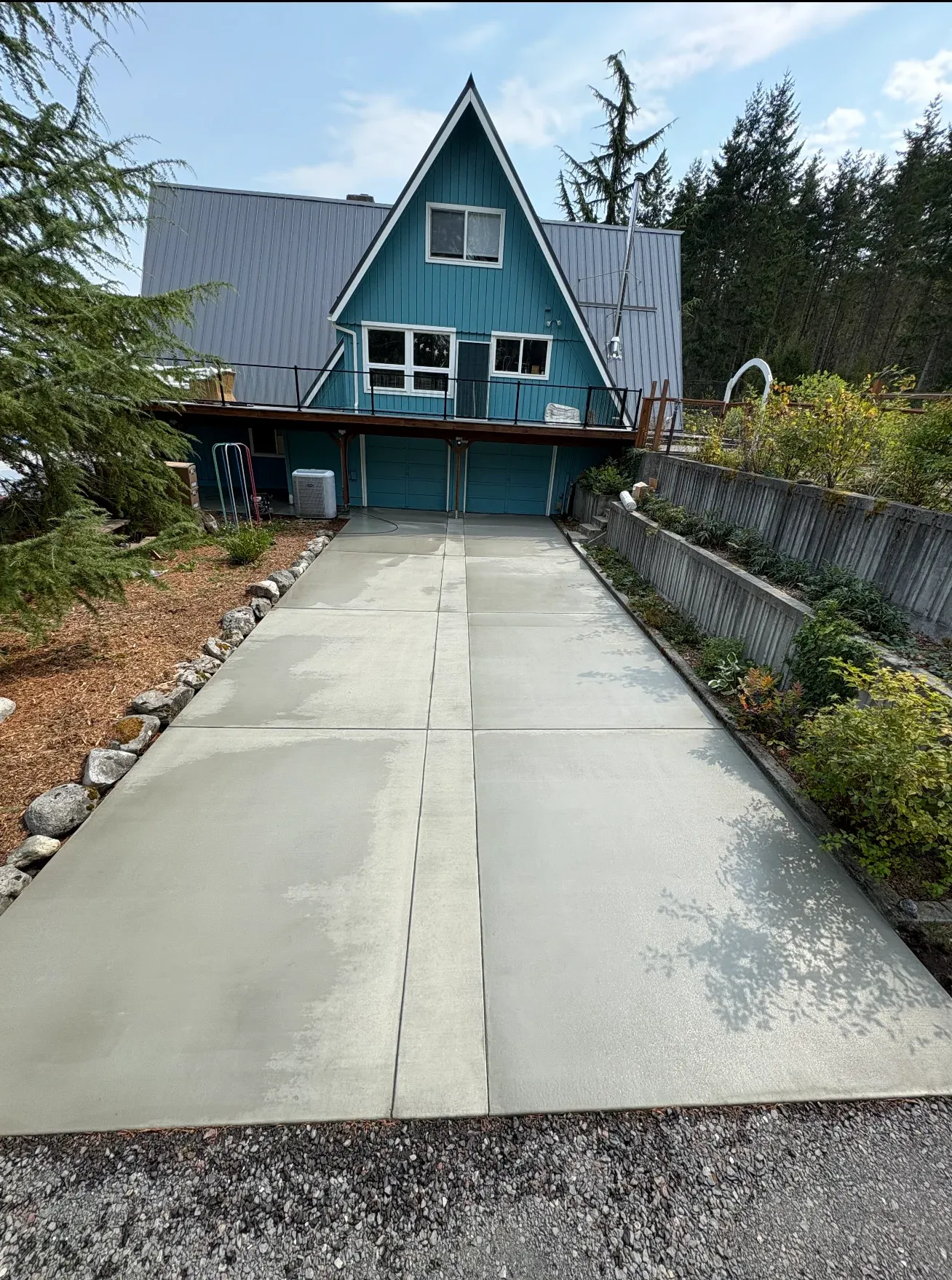 Blue A-frame house with concrete driveway surrounded by trees and greenery